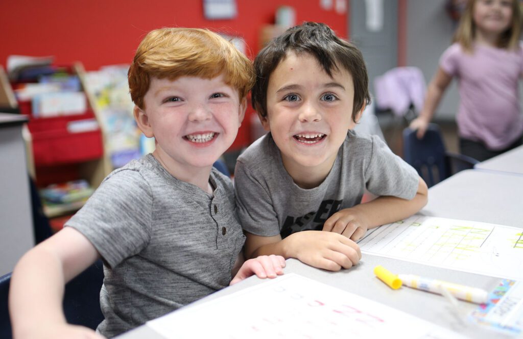 Two boys at a table leaning in and smiling